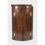 EARLY NINETEENTH CENTURY INLAID MAHOGANY BOW FRONTED CORNER CUPBOARD, of typical form with oval