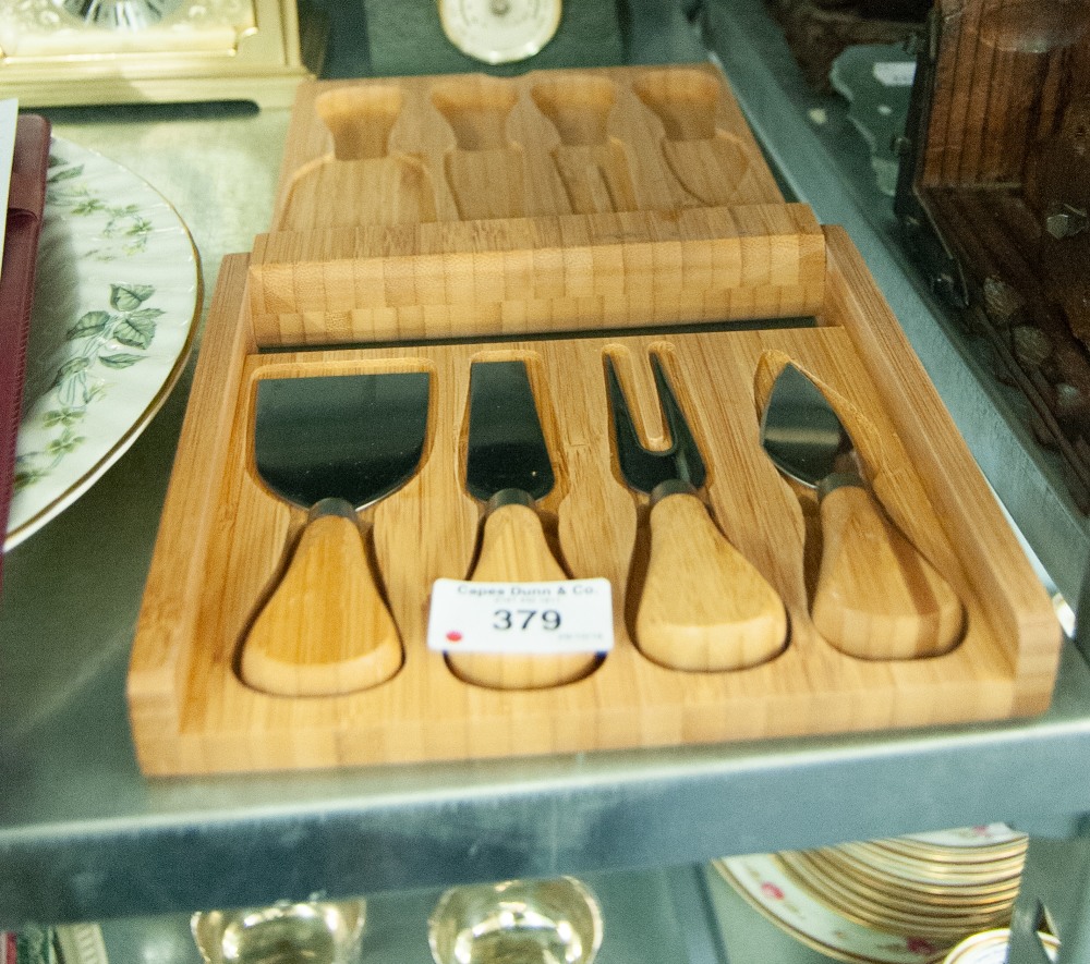 A WOODEN FOLDING CHEESE BOARD CONTAINING FOUR CHEESE IMPLEMENTS