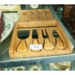 A WOODEN FOLDING CHEESE BOARD CONTAINING FOUR CHEESE IMPLEMENTS