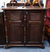 AN EDWARDIAN OAK CUPBOARD HAVING TWO DOORS WITH LOW RELIEF CARVED DETAIL TO FOUR PANELS, ENCLOSING