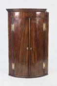 EARLY NINETEENTH CENTURY INLAID MAHOGANY BOW FRONTED CORNER CUPBOARD, of typical form with oval