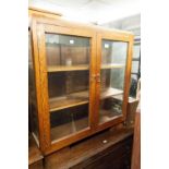 AN OAK AND GLASS TWO DOOR SMALL BOOKCASE/DISPLAY CABINET