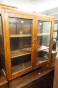 AN OAK AND GLASS TWO DOOR SMALL BOOKCASE/DISPLAY CABINET