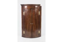 EARLY NINETEENTH CENTURY INLAID MAHOGANY BOW FRONTED CORNER CUPBOARD OF TYPICAL FORM WITH OVAL SHELL