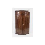 EARLY NINETEENTH CENTURY INLAID MAHOGANY BOW FRONTED CORNER CUPBOARD OF TYPICAL FORM WITH OVAL SHELL