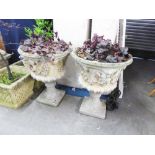 A PAIR OF COMPOSITION GARDEN URNS WITH HEAD DECORATION TO THE SHALLOW BOWLS, ON SWEPT PEDESTALS (2)