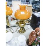 AN ADAPTED OIL LAMP WITH ORANGE GLASS GLOBE AND CLEAR GLASS FUNNEL