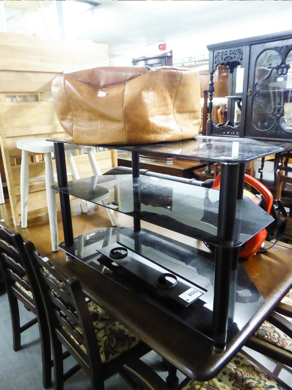 A BLACK GLASS THREE TIER TELEVISION STAND AND A TOOLED LEATHER CIRCULAR POUFFE