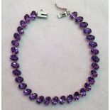 A 9ct white gold and amethyst line bracelet, the oval cut amethysts obliquely set in claw mounts.