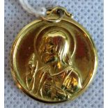 A circular yellow metal pendant depicting the Madonna and Child to one side and Jesus giving a