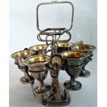 A silver breakfast set consisting of six egg cups and four spoons on stand.