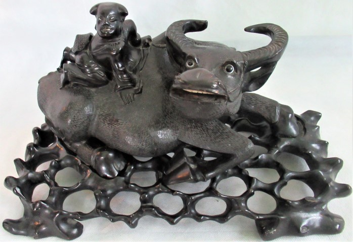 A 20th century carved hardwood figure of a recumbent water buffalo with an Oriental gentleman on