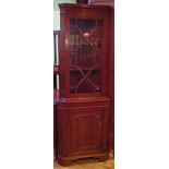 A reproduction mahogany two tier corner cupboard, with astragal glazed door above blind door.