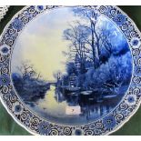 A late 19th/early 20th century blue and white Delft charger, depicting a river and woodland scene,