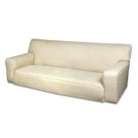 Betty Joel, a large cream upholstered modernist sofa, with squared arms and raised on casters 84 x
