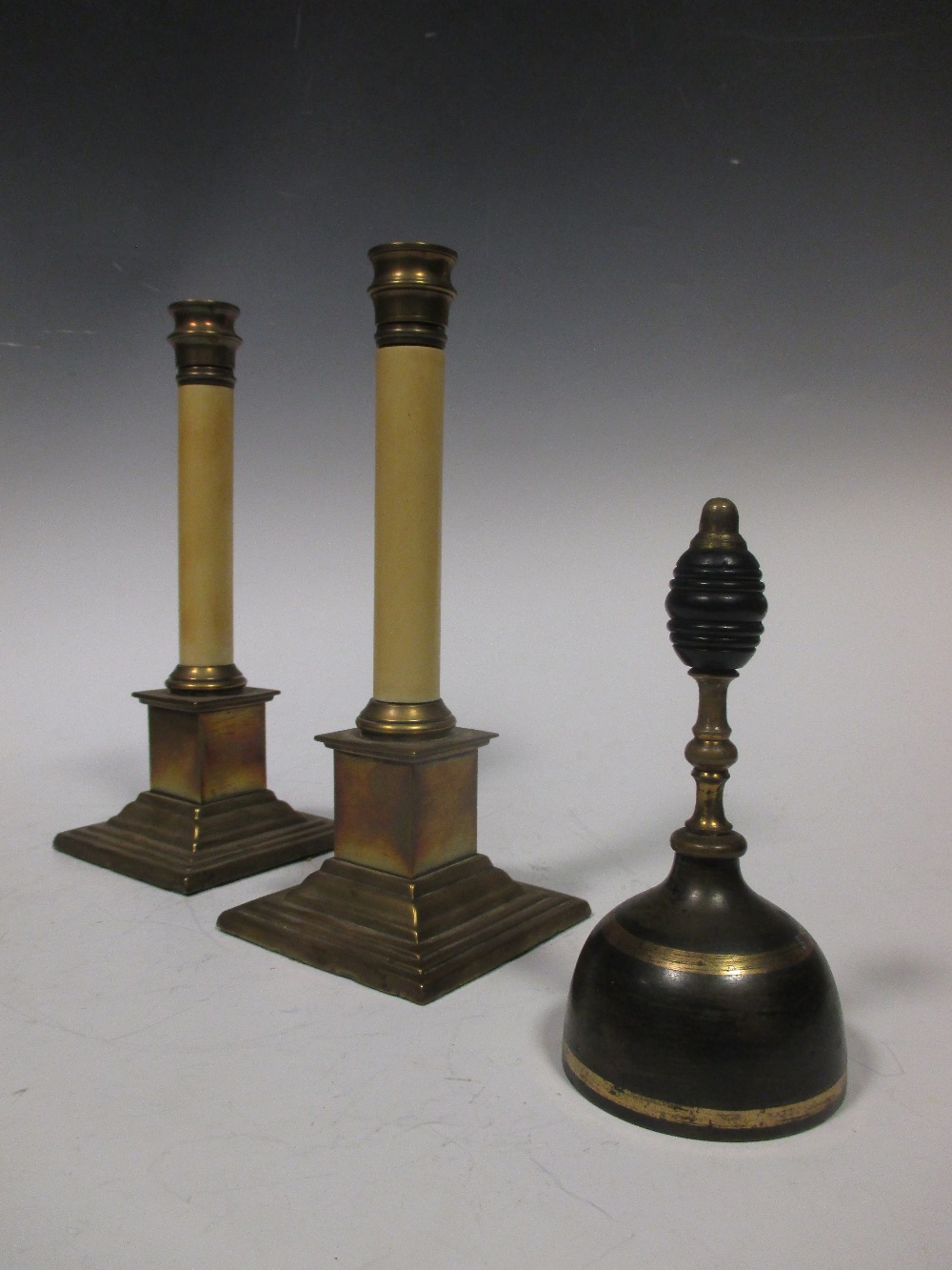 A pair of brass footed white columnar candlesticks and a handbell together with a quantity of