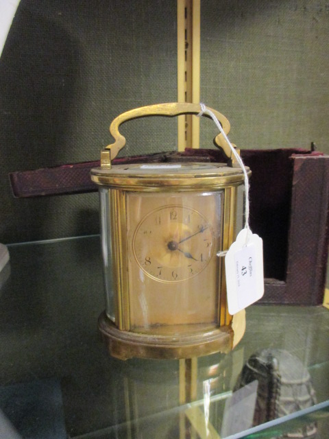 An Edwardian gilt carriage clock, the glazed oval body with swing handle, Arabic numerals complete