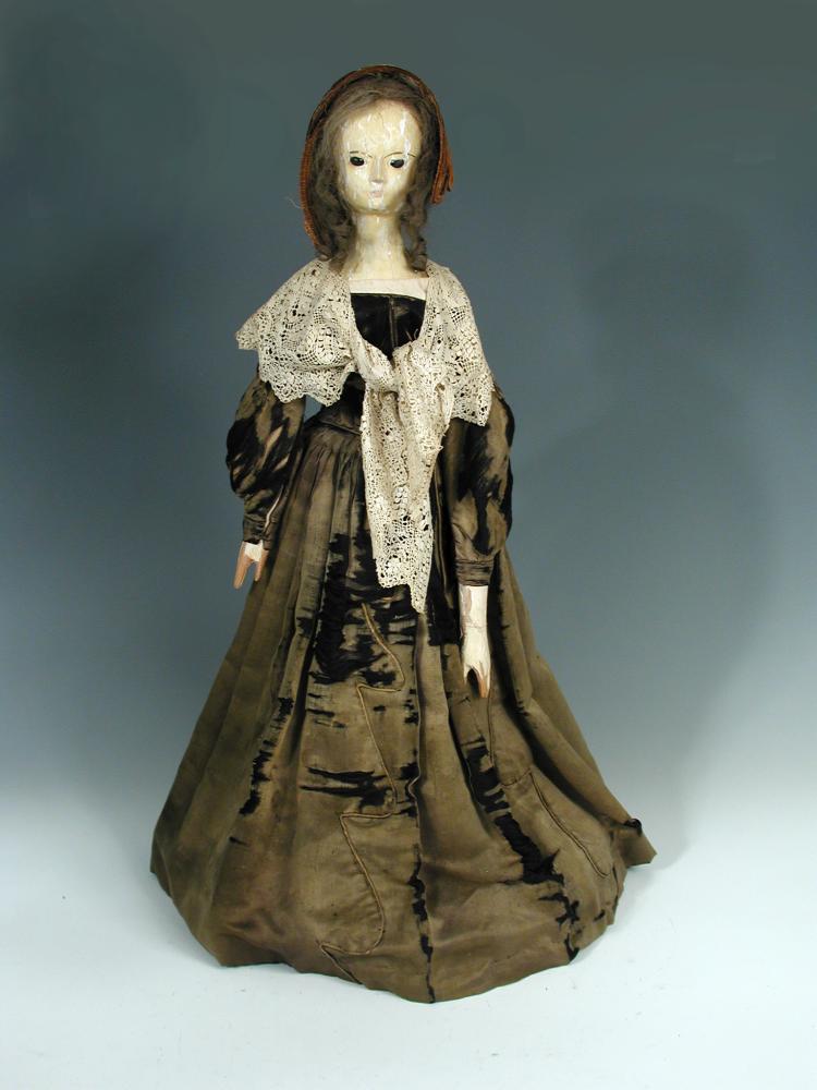 Miss Timber', an 18th century painted wood doll, she wears a lace shawl over her brown silk dress,