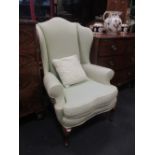 A pair of green upholstered wing back armchairs on cabriole legs