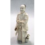 An early 20th century ivory figurine of a samurai, he stands with his right hand on his long sword