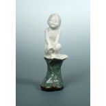 An unusual Doulton Lambeth model of a young child perched upon a rock, the white glazed figure to