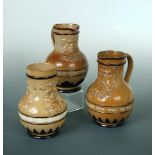 Two similar Doulton stoneware mask jugs and a similar vase, the jugs inscribed 'Fill What You Will