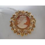 A circular brooch/pendant with a central cameo bordered by foliate decoration. Yellow metal tests to