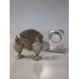 A small silver clock with an enamelled dial; two silver peperettes and a small silver sewing box/pin