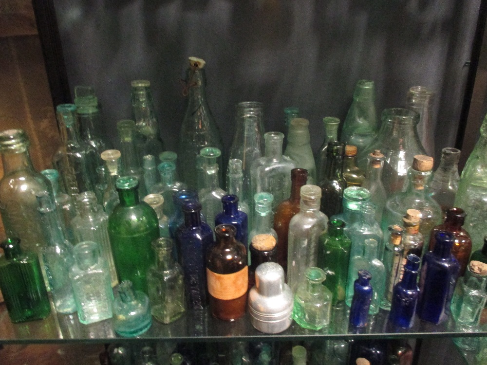 A very large quantity of glass bottles of varying sizes, salt glazed jars and various oil lamps