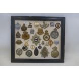 A framed display of 28 military badges; all appear to retain their fixings to the reverse.