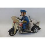 A tinplate model of a police patrol figure astride a three wheeler motorcycle, made by Nomura,