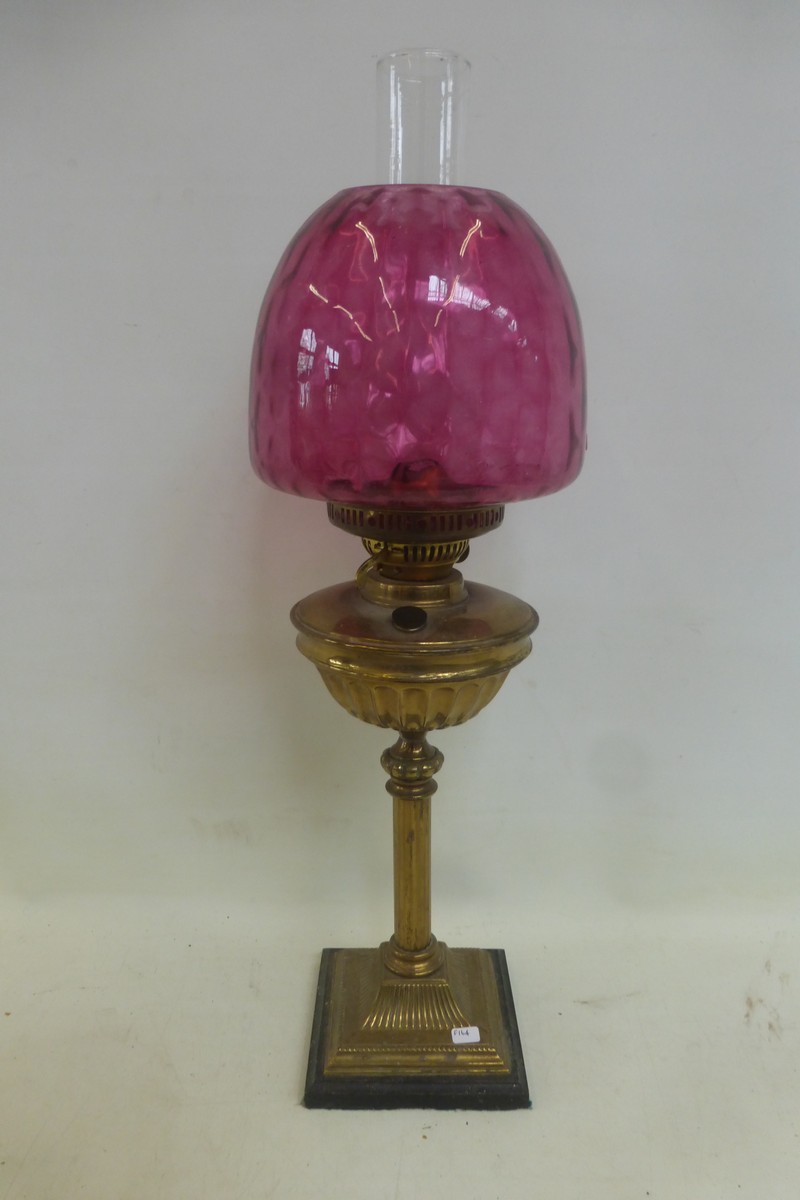 A brass oil lamp of classical form, with a cranberry glass shade.