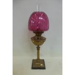 A brass oil lamp of classical form, with a cranberry glass shade.