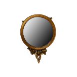 A Regency giltwood and gesso convex wall mirror, early 19th Century, the circular plate over a Ram's