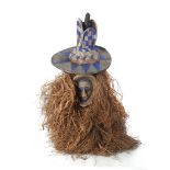 A YAKA MASK The small painted mask is surrounded by an over-sized raffia collar and is topped with a