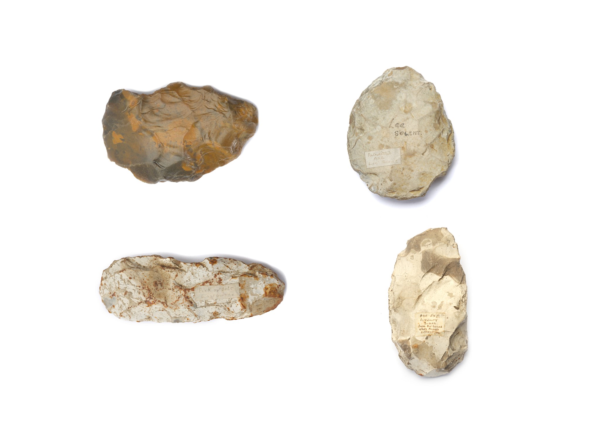 A GROUP OF PREHISTORIC IMPLEMENTS Including a large hand axe with a pale grey surface, curved at