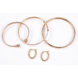 A small group of jewellery, comprising three 9ct gold bangles and a pair of 9ct gold earhoops, UK