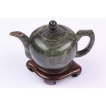 A Chinese green hardstone teapot and cover, 20th century, of compressed globular form, on a hardwood