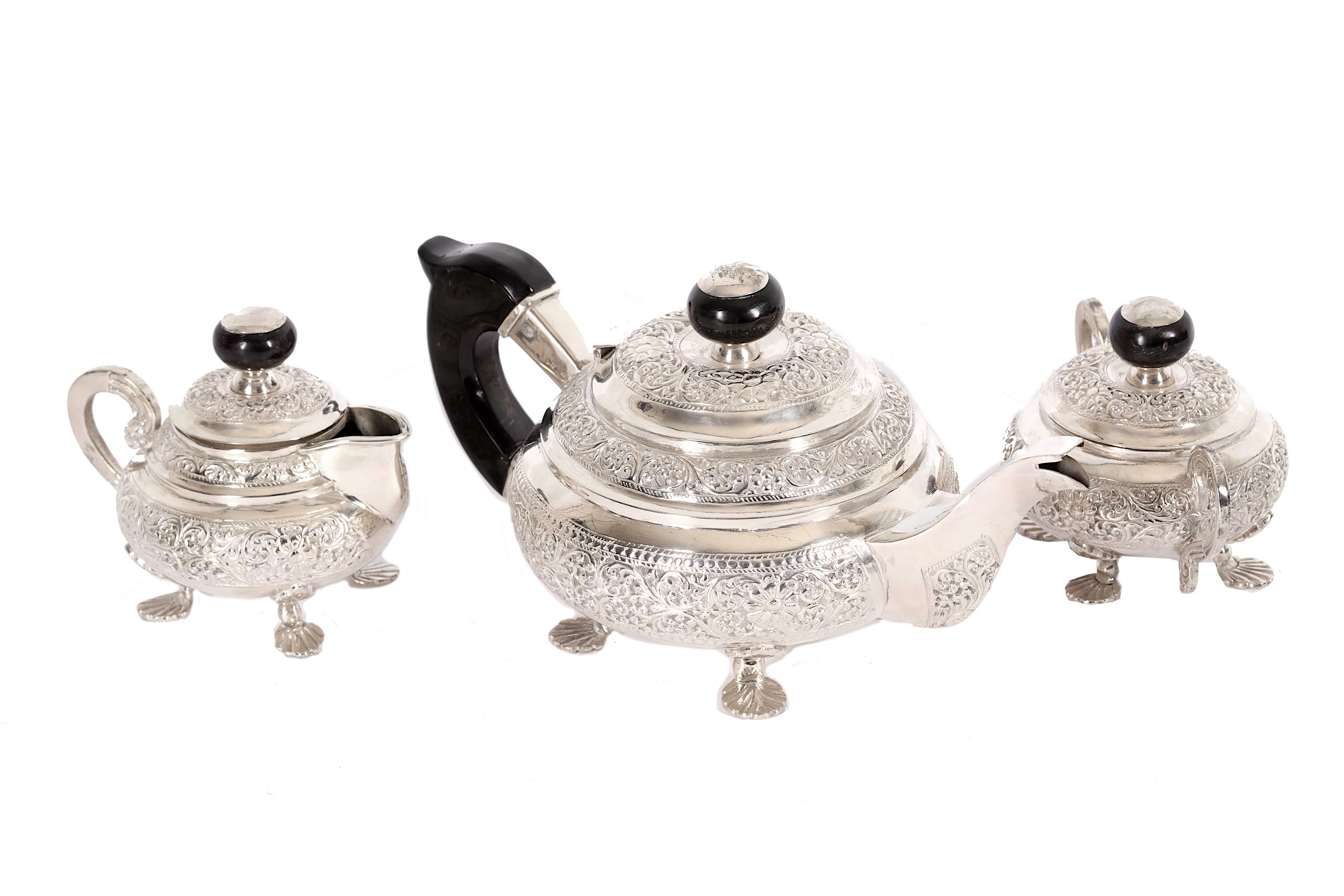 An Indian embossed white metal three-piece tea set, with ebonised mounts (3)