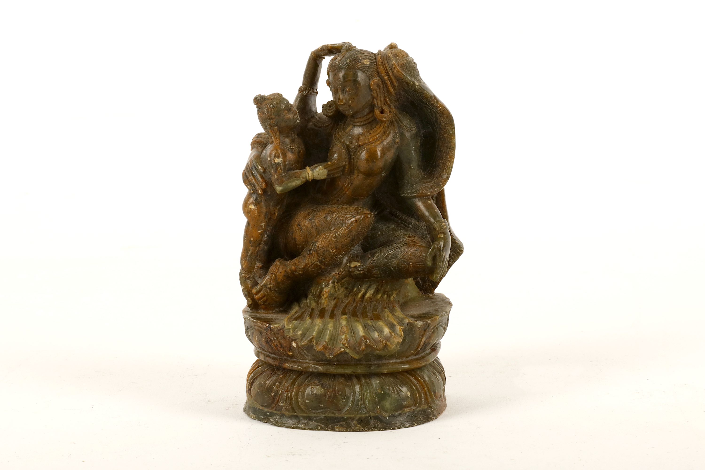 An Indian soapstone carving of a figurative group, depicting with a female figure sitting on a lotus