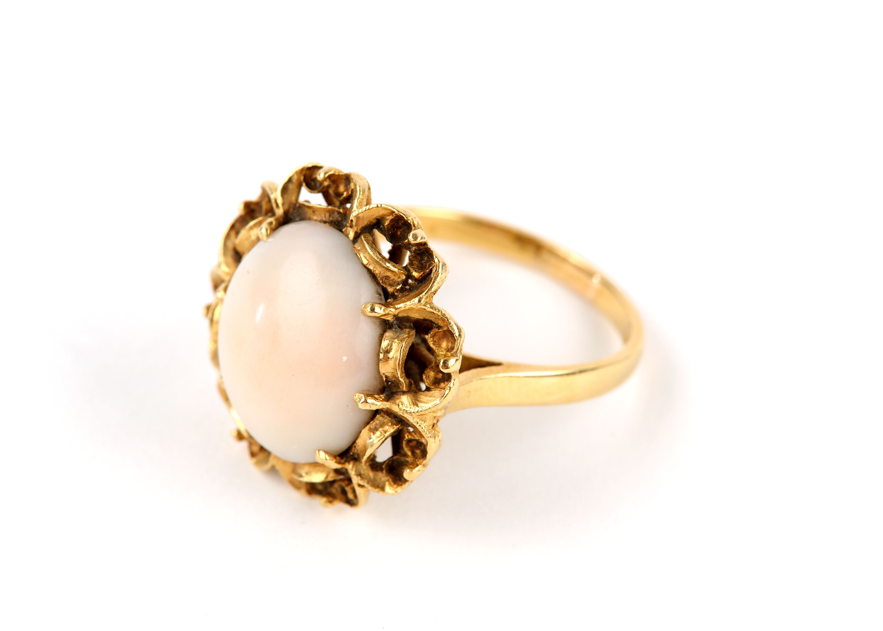 A coral ring, the oval cabochon coral Corallium rubrum, within a scrolling gallery, stamped 750,