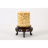 A carved Chinese ivory brush pot and wood stand, 19th Century, of cylindrical form, the exterior