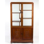 A Chinese display cabinet with glazed front and back, fitted shelves above carved panel doors,