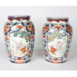 A pair of Japanese Imari vases, decorated reserves of figures to a scrolling foliate ground,