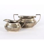 A silver sugar basin and cream jug, London 1910, of half ribbed form,