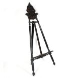 A carved and ebonised floor standing easel, the crest carved eagle heads, fruits and scrolls,