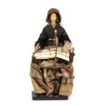 A Victorian pedlar doll wearing a straw bonnet and carrying a full basket of goods, set on a stand,