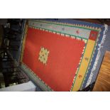 A Peruvian rug, worked with a central figural motif to a red ground,