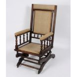 A late Victorian beech framed rocking chair with turned spindle supports and upholstered seat,