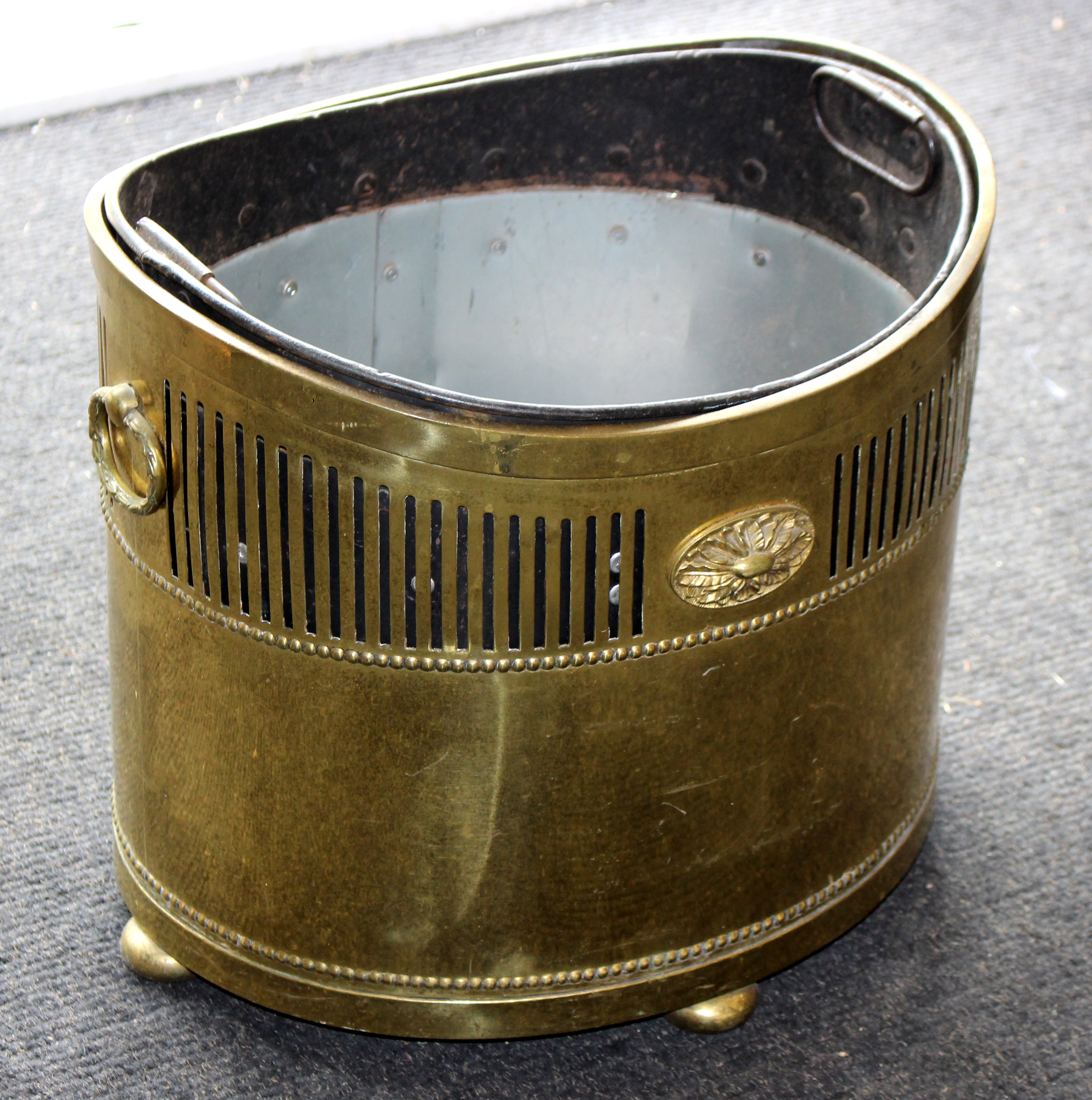 A brass coal scuttle of oval shape with pierced sides and ring handles